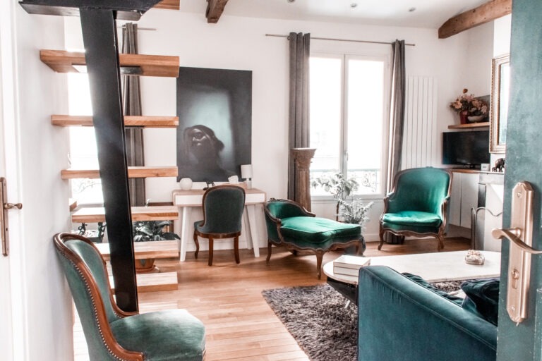 Apartment rental in Le Marais Paris showing blue and green velvet chairs, sofa with marble fireplace and tables
