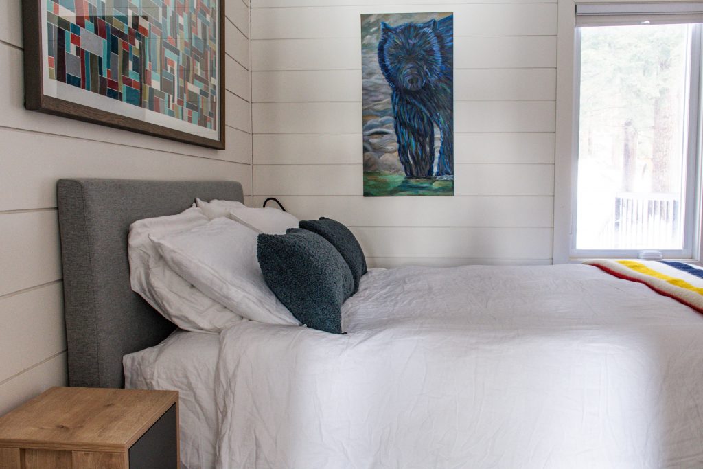 bedroom with white bedding, gray headboard, artwork in Scandinavian Muskoka Cottage 