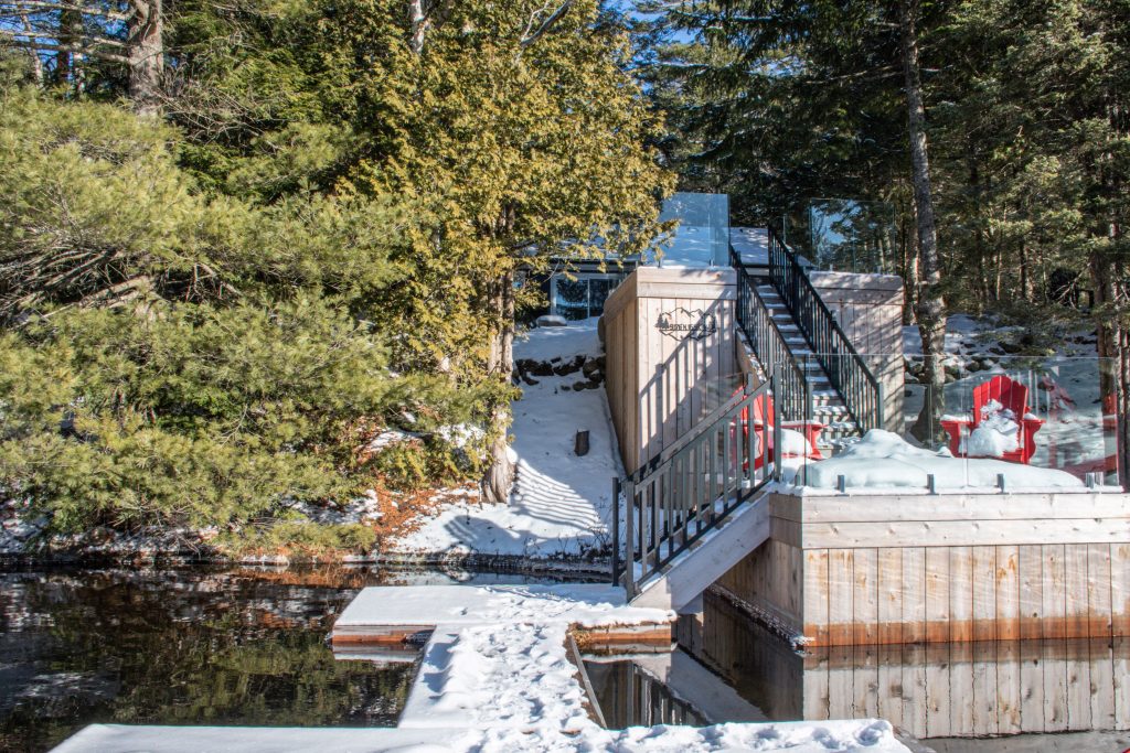 floating dock with red Muskoka chairs with trees at Muskoka cottage in winter with snow